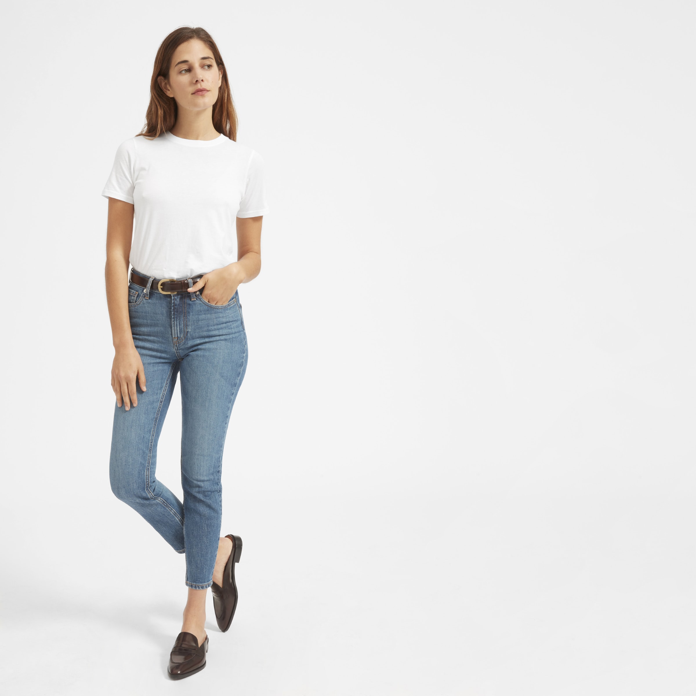 Девушка на белом фоне в белой футболке, джинсах и кроссовках