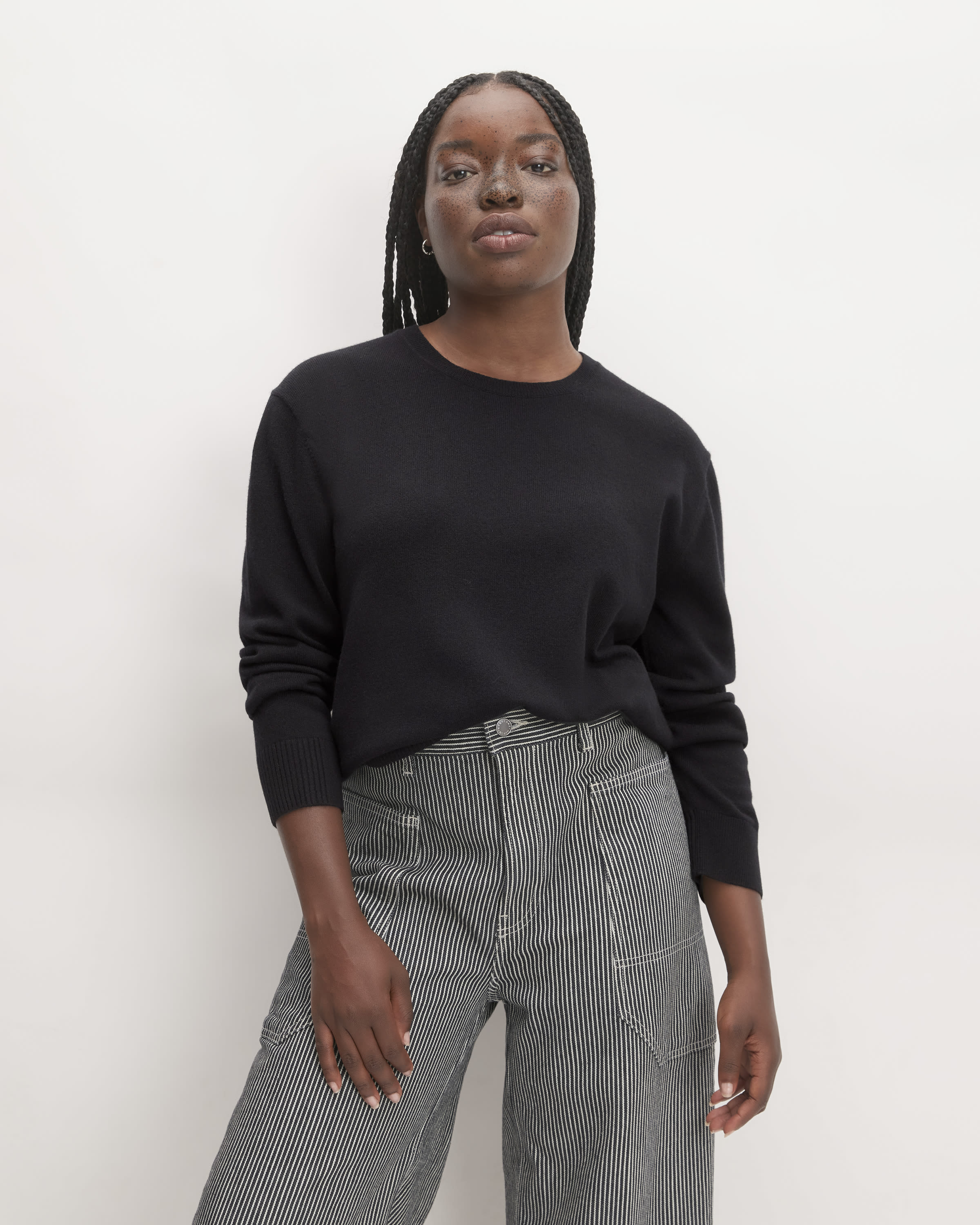 Model wearing a black cashmere classic crew sweater paired with high-waist black and white striped pants